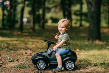 Mavi tişörtlü, mavi şortlu, kısa saçlı beyaz bir çocuk yaz parkında çok vakit geçirir..