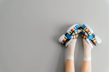 Gri arka planda renkli yüksek kama deri sandaletlerle poz veren beyaz çoraplı güzel kadın bacakları. Kadınların modern moda moda ayakkabıları. Yüksek topuklu ayakkabı giyen bir kız..