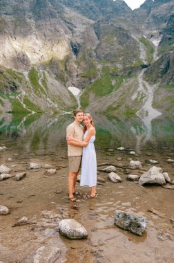 Soğuk gölde sarılan genç çift yaz günü yüksek dağların arasında..