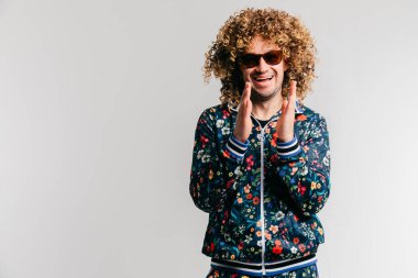 80 'lerin kıyafetleri içinde yetişkin bir adamın portresi. Gülümseyen, kıvırcık saçlı, gülen, mutlu çocuk gibi el çırpan neşeli bir erkek. Neşeli duyguları olan olumlu bir çocuk stüdyoda beyazlar içinde izole edilmiş..