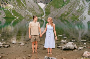 Soğuk gölde sarılan genç çift yaz günü yüksek dağların arasında..