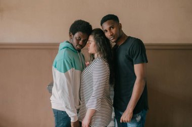 Çok kültürlü aşk ve ilişkiler kavramı. Genç beyaz kadın iki koyu tenli Afrikalı adamın arasında duruyor. Irklar arası aşk üçlüsünün kapalı bir portresi. İki Afrikalı erkek, sevgililerine sarılıyor.