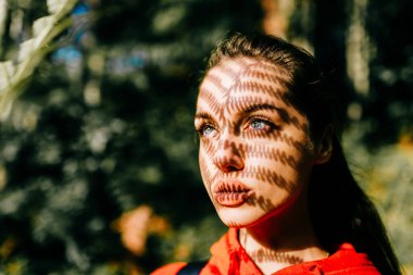 Sanat yaşam tarzı, doğadaki garip, oldukça uzun saçlı kızın yakın plan portresi. Eğrelti otu dalından düşen güneş ışığının güzel gölgesi olan çekici bir genç.