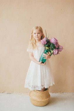 Sarı arka planda saman sepetinde duran beyaz elbiseli güzel, uzun saçlı kız çocuğu. Elinde bir buket çiçekle elinde vazo tutan güzel bir kadının ev yapımı portresi.