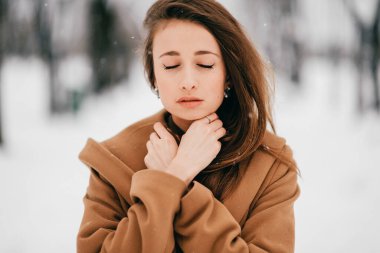 Gürcü görünümlü güzel, uzun saçlı esmer kız portresi kış parkında kahverengi ceketle poz veriyor.