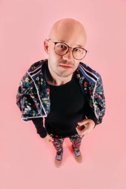 Gözlüklü tuhaf, çılgın kel adamın tuhaf portresi farklı duygular gösteriyor. Yüz ifadesi. Şık çocuk pembe arka planda çiçek desenli şık eşofman giyiyor..