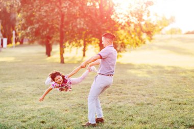 Babam kızımsı elini bacağıyla tutuyordu ve dönüyordu. Heyecanlı aile yaz parkında iyi eğlenceler. Babam yeşil çayırda küçük kız çocuğuyla oynuyor. Kaygısız mutlu bir çocukluk. Babalık 