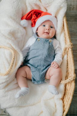 Mavi pijamalı neşeli küçük bebek beyaz yorganın üzerinde yatıyor.