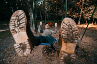 Garip, tuhaf, tuhaf insanlar konsepti. Çocuk parkında salıncakta sallanan pahalı, modaya uygun botları olan yetişkin bir adam. Çok komik bir fikir. Çocuk içeride. Bacaklarını aç.
