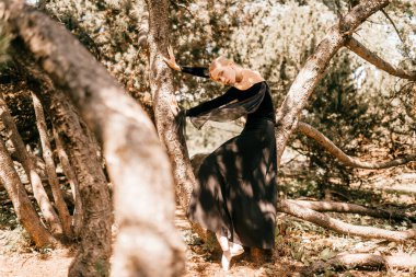 Siyah bir elbise içinde, ağaçların arasında poz vermiş güzel bir balerin..