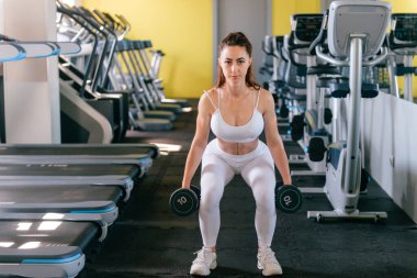 Güzel vücutlu kaslı genç bir kadın halterle egzersiz yapıyor. Sportif kız spor salonunda ağırlık kaldırıyor.