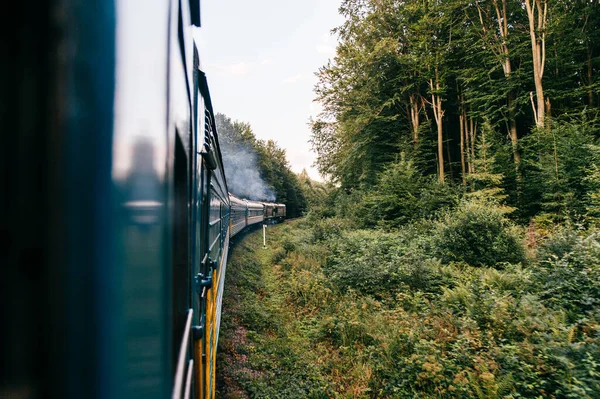 Landscape beautiful view out of window from riding train among summer nature with hills, mountains and forest. Vacation and travel concept. Locomotive with train cars moving along railroad track