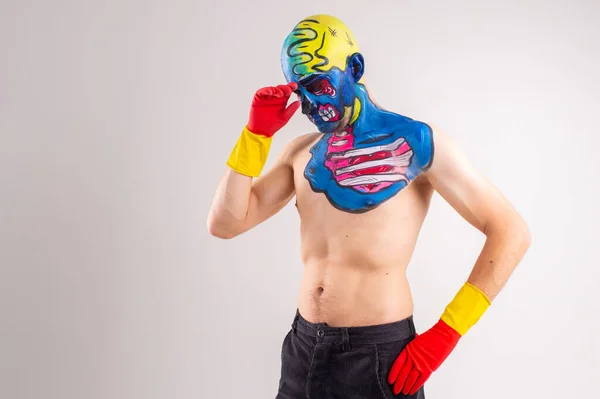 Portrait of a strange man with makeup on his head and shoulder in red-yellow gloves, black pants and boots, no T-shirt