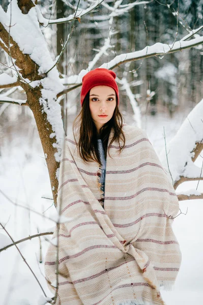 年轻迷人的姑娘 披着温暖的斗篷 站在森林的雪枝间 — 图库照片