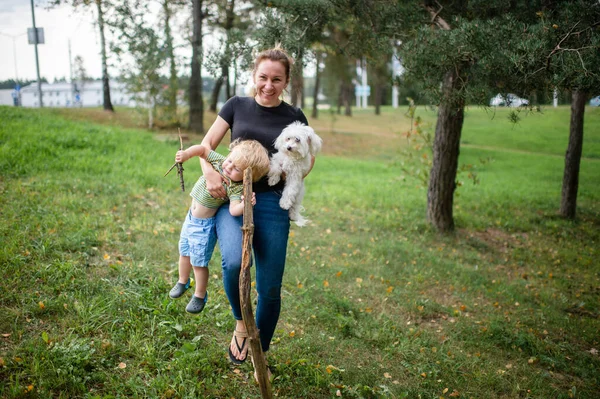 Boldog Anya Hordozza Kisgyermekét Fehér Kutyáját Parkban — Stock Fotó