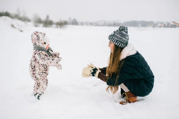 若い美しい母親は冬に小さな娘と屋外で遊んでいます 美しい子供を持つ幸せな陽気な笑顔の女性は雪の中で楽しんでいます 母親と子供の頃 赤ちゃんを持つ親 一緒に — ストック写真