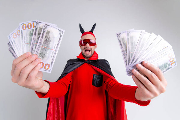Devil man in halloween costume demonstrating lots of money in his hands over white studio background.