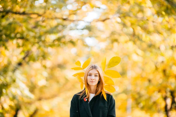 strange Young girl in black coat with autumn leaves behind her head in nature on blurred yellow background. work of art by a romantic woman. strange lady in autumn in autumn Park. portrait on a belt