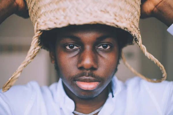 Closeup lifestyle portrait of strange young african black man holding straw basket above his head on abstract background and looking at camera. Dark-skinned nigerian boy indoor funny mood portrait.