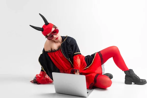 セクシーブルネット女性で赤タイツ 黒ブーツと悪魔角でラップトップ以上ホワイトスタジオ背景 — ストック写真