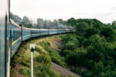 Yaz doğası arasında trene binme fotoğrafı. Pencereden dışarı bak. Trenle seyahat ediyorum. Demiryolu dönüşü. Tatile gidiyorum. Turizm ve seyahat. Demiryolu açık havada. Eski arabalarla hareket eden klasik lokomotif