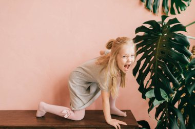 Beyaz taytlı, güzel, uzun saçlı bir kız çocuğu. Pembe duvarda heyecanlı bir suratı olan vahşi bir kaplan gibi poz veriyor. Yüce dişi çocuk ormanda çığlık çığlığa vahşi kedi gösteriyor.