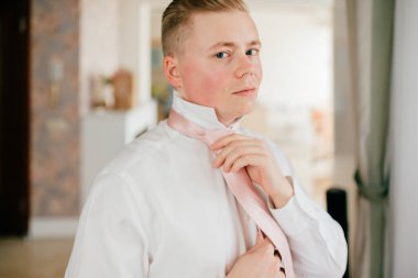 Genç damat hazırlanıyor. Nişanlısı sabah evde. Damat kravatını düzeltiyor..