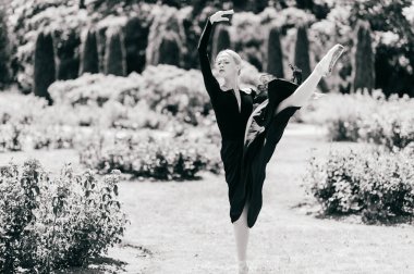 Siyah elbiseli genç balerin yaz parkında poz veriyor ve bale yapıyor.