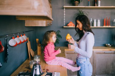 Sevimli genç bayan mutfakta komik kızıyla oynuyor. Güzel bir annenin portresi kucağında taşıdığı ve küçük dişi çocuğunu izlediği. Mutlu aile içinde yaşam tarzı portresi.