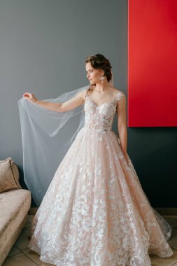 Gri arka planda, elinde çiçekle poz veren beyaz elbiseli güzel gelinin portresi.