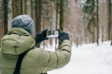 Kış ormanlarında erkeklerin elinde akıllı telefon. Güneşli kış günü. Cep telefonu tutan ve fotoğraf çeken bir adam. Bulanık karlı ormanda cep telefonu..