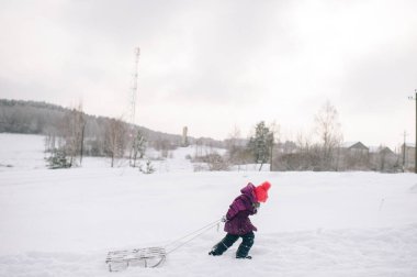 Küçük bir çocuk soğuk kış gününde kızağı çekiyor..
