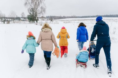 Karlı bir günde kızaklara binmek için çocuklarıyla birlikte tarlada yürüyen dost canlısı bir aile. Kış eğlencesi.