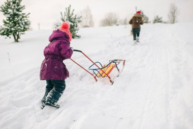 Küçük bir kız kızağı açık havada kar kaydırağına itiyor. Kış çevrelemesi.