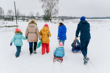 Karlı bir günde kızaklara binmek için çocuklarıyla birlikte tarlada yürüyen dost canlısı bir aile. Kış eğlencesi.