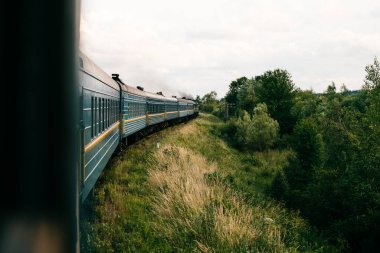 Yaz doğası arasında trene binme fotoğrafı. Pencereden dışarı bak. Trenle seyahat ediyorum. Demiryolu dönüşü. Tatile gidiyorum. Turizm ve seyahat. Demiryolu açık havada. Eski arabalarla hareket eden klasik lokomotif