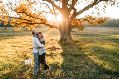 Sonbahar tarlasında gün batımında yürüyen ve kucaklaşan genç çift.