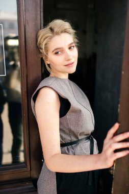 Yalnız, güzel, sevimli, çekici, genç, model sarışın, zarif yüzlü, şık elbiseli kızın portresi kafe girişinin önünde duruyor ve etrafa bakıyor. Saf güzellik ve şefkat.