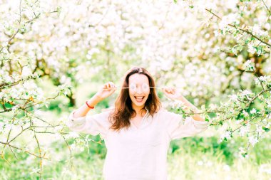 Genç, mutlu, gülümseyen ve gülen uzun saçlı güzel esmer kız portresi. Parkta tatilin tadını çıkarıyor. İki karahindiba ile gözlerini gizleyen bir kadın. Bil bakalım kim. Görünmez yaşam