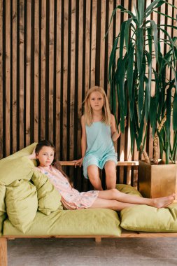 İki küçük dikkatsiz kız iç stüdyoda rahat bir şekilde şık elbiseler giyip kameraya bakıyorlar..