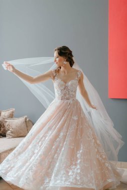 Gri arka planda, elinde çiçekle poz veren beyaz elbiseli güzel gelinin portresi.