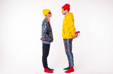 Tarz sahibi bir adam beyaz arka planda renkli elbiseli bir kız arkadaştan hediye saklıyor.