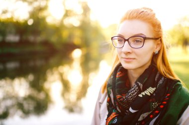 Ensesinde alışılmadık bir atkısı olan kızıl saçlı çekici genç kadın güneşli bir günde doğada duruyor. Sonbaharda göl kenarında zarif genç elbiseleriyle gezen, gözlüklü, zayıf bir kadın..
