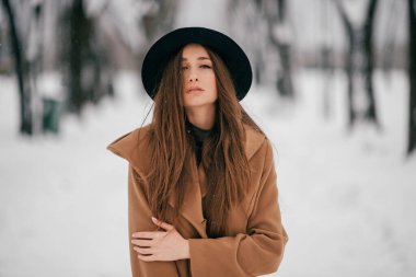 Gürcü görünümlü güzel, uzun saçlı esmer kız portresi kış parkında kahverengi ceketle poz veriyor.