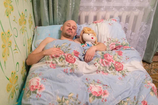 成年秃头男人睡在床上 抱着布娃娃和懒猫 寂寞的人的概念宠物情人 与小猫和玩具一起睡在沙发上的快乐男人 — 图库照片