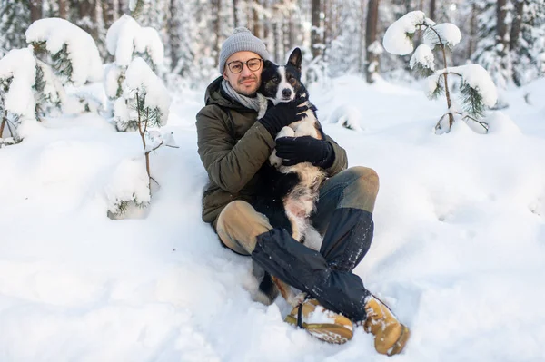 Happy man holding lovely dog in his hands in snowy forest. Smiling boy hugging adorable puppy in winter wood. Pet lover.  Dog - human`s friend concept.