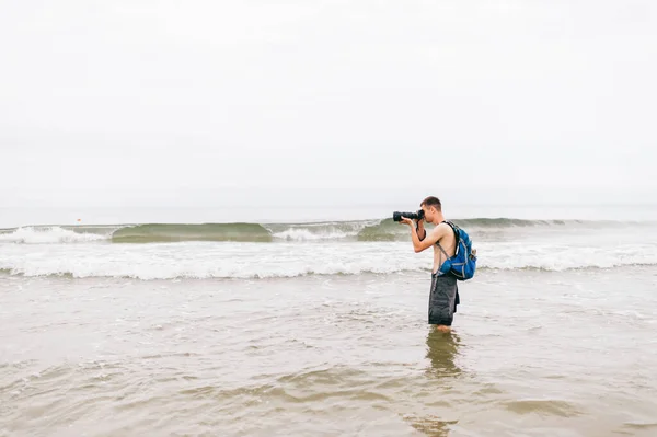 Молодой Человек Шортах Рюкзаке Позади Преклоняет Колени Пляже Фотографирует Угодно — стоковое фото