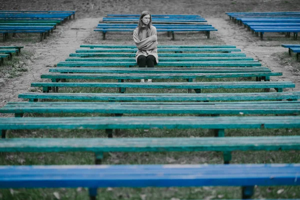 忧郁的女孩一个人坐在公园的长椅上 身边有许多荒凉的长椅 孤独和绝望的概念 — 图库照片