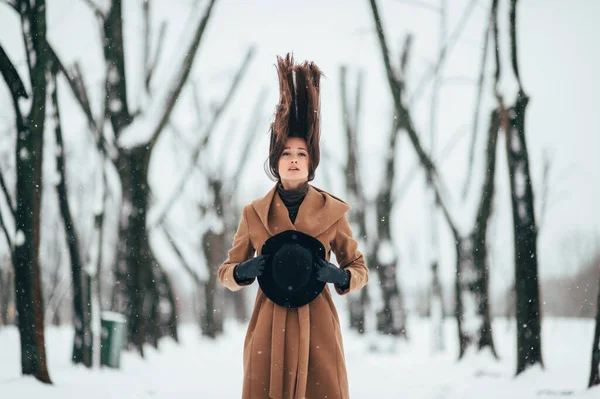 Unusual portrait of beautiful girl with dramatic face holding her hat and trowing up her hair in winter tree valley