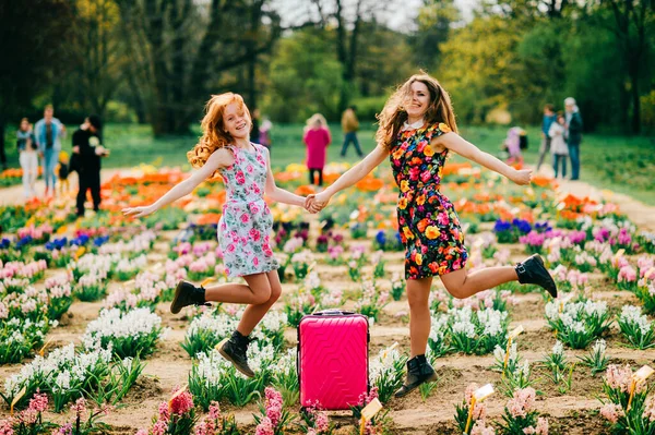 魅力的な子供とともに長い赤髪喜びとともに彼女のかなり背の高い妹リラックスと喜びで大花の庭で週末 — ストック写真